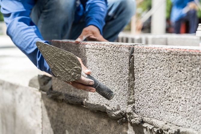 Worker spreading mortar on a concrete block wall with a trowel