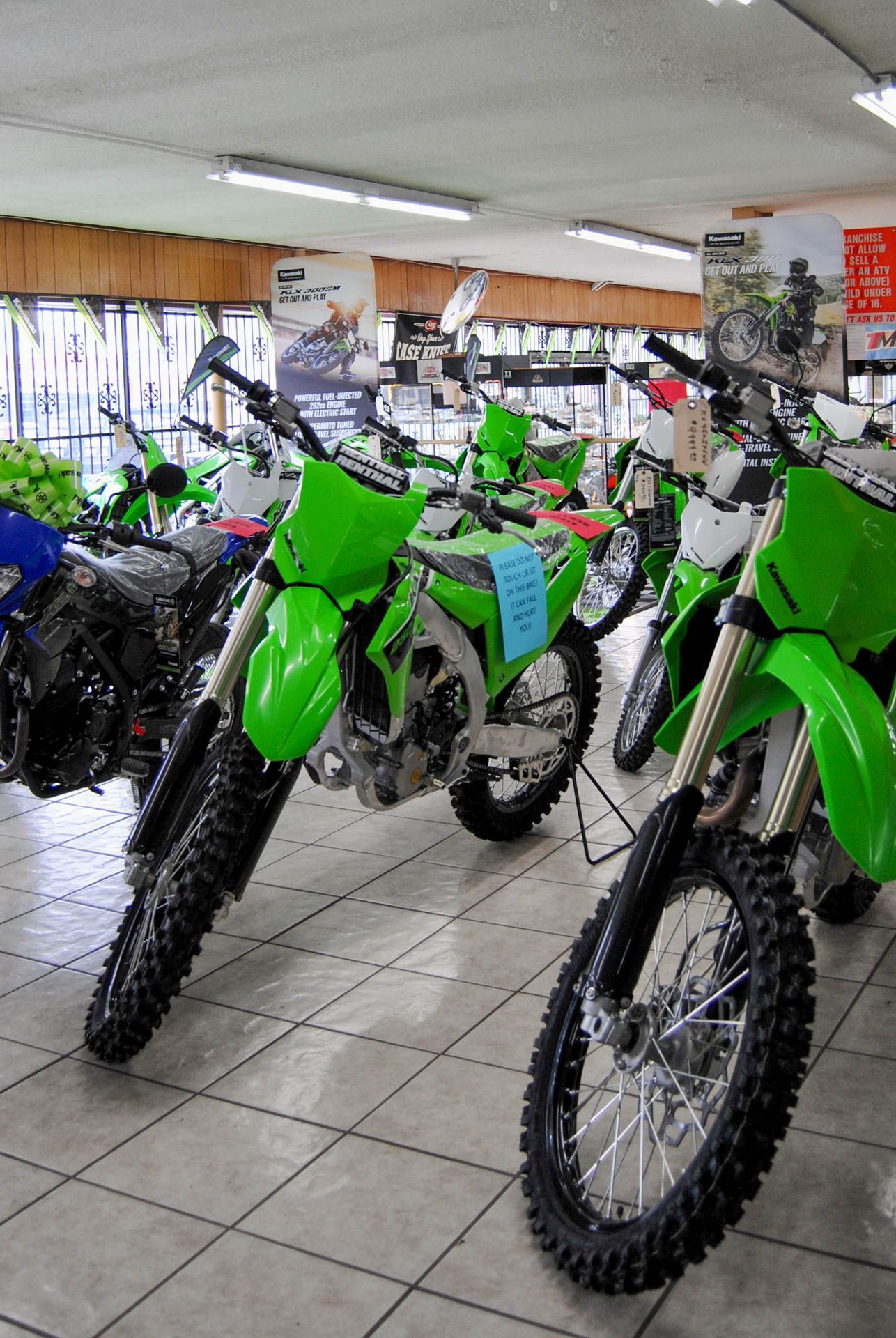 A row of green dirt bikes are parked in a showroom.