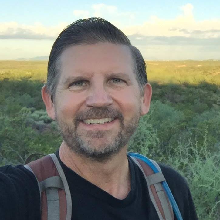 A man with a beard and a backpack is smiling for the camera.