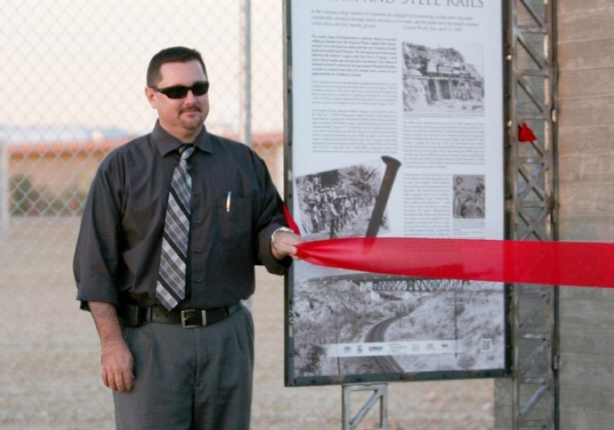 A man in a black shirt and tie is cutting a red ribbon