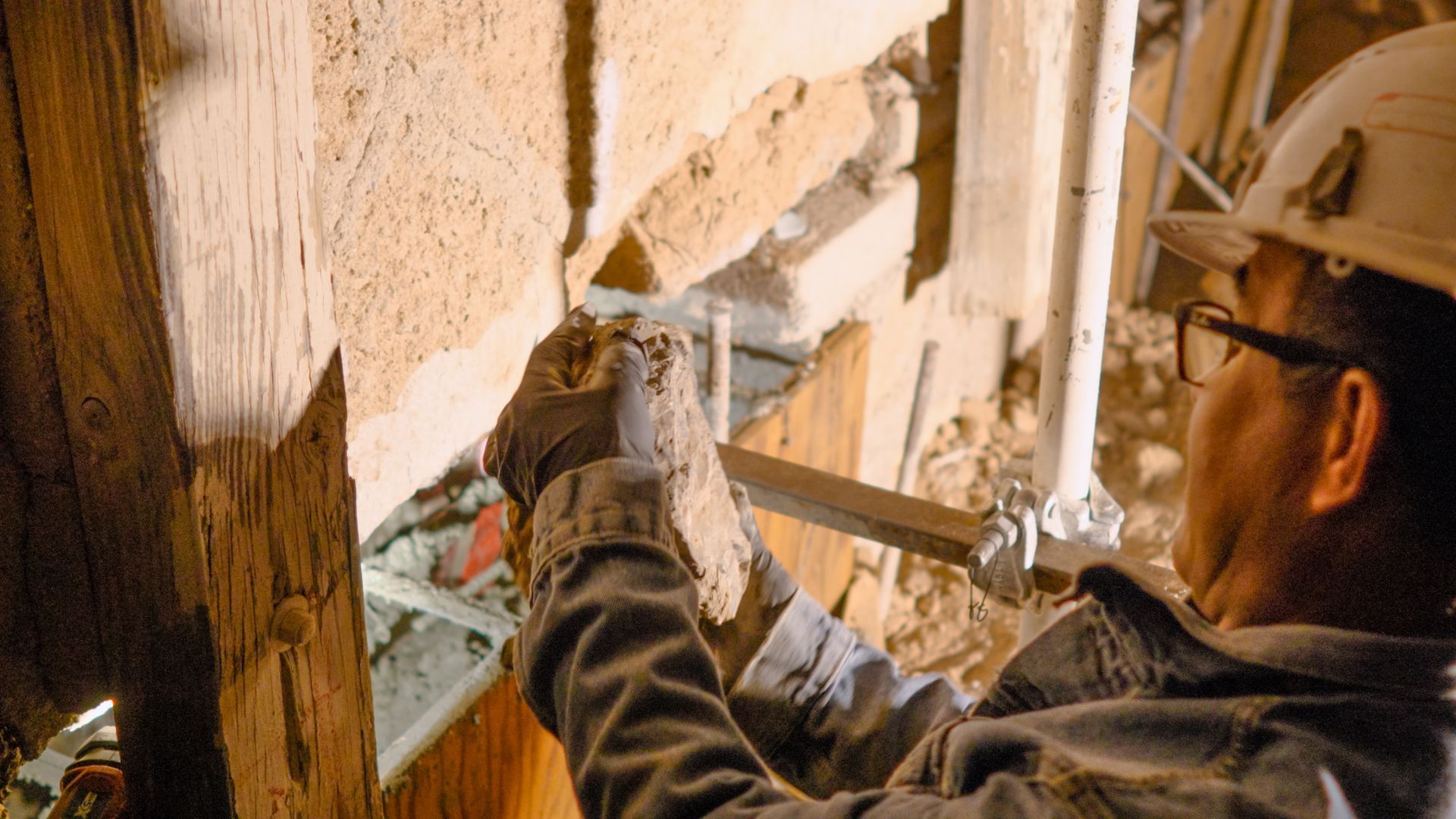 Construction worker in a hard hat and gloves working on a wooden structure, possibly restoration work.