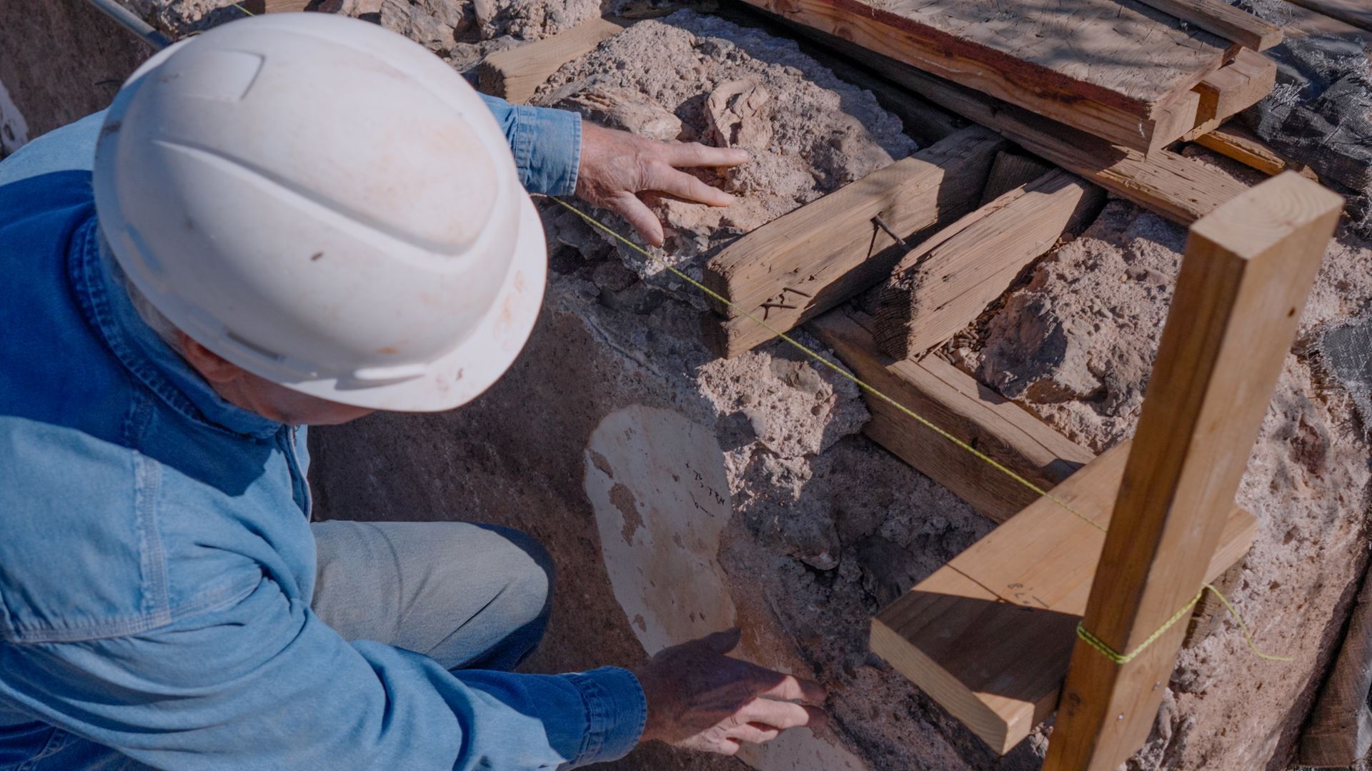 Person in hard hat examining a rock formation with wooden support structure.