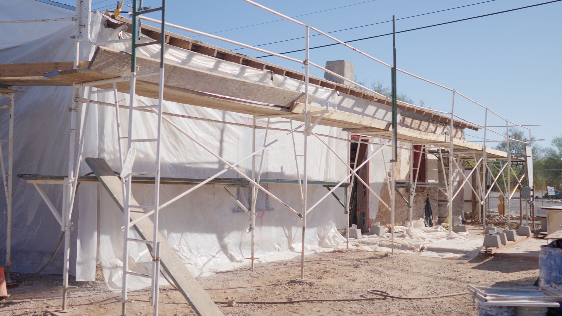 Building under construction, scaffold, white tarp, brown dirt.