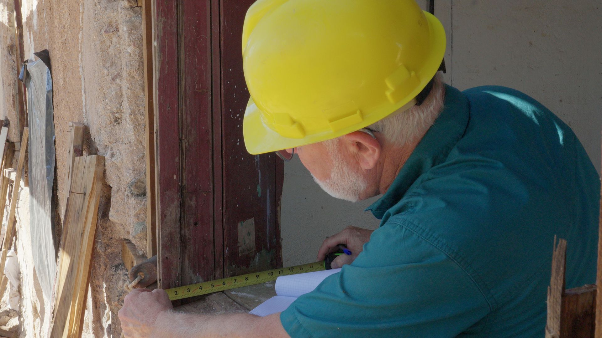 Person in yellow hard hat measuring a doorway with a tape measure.