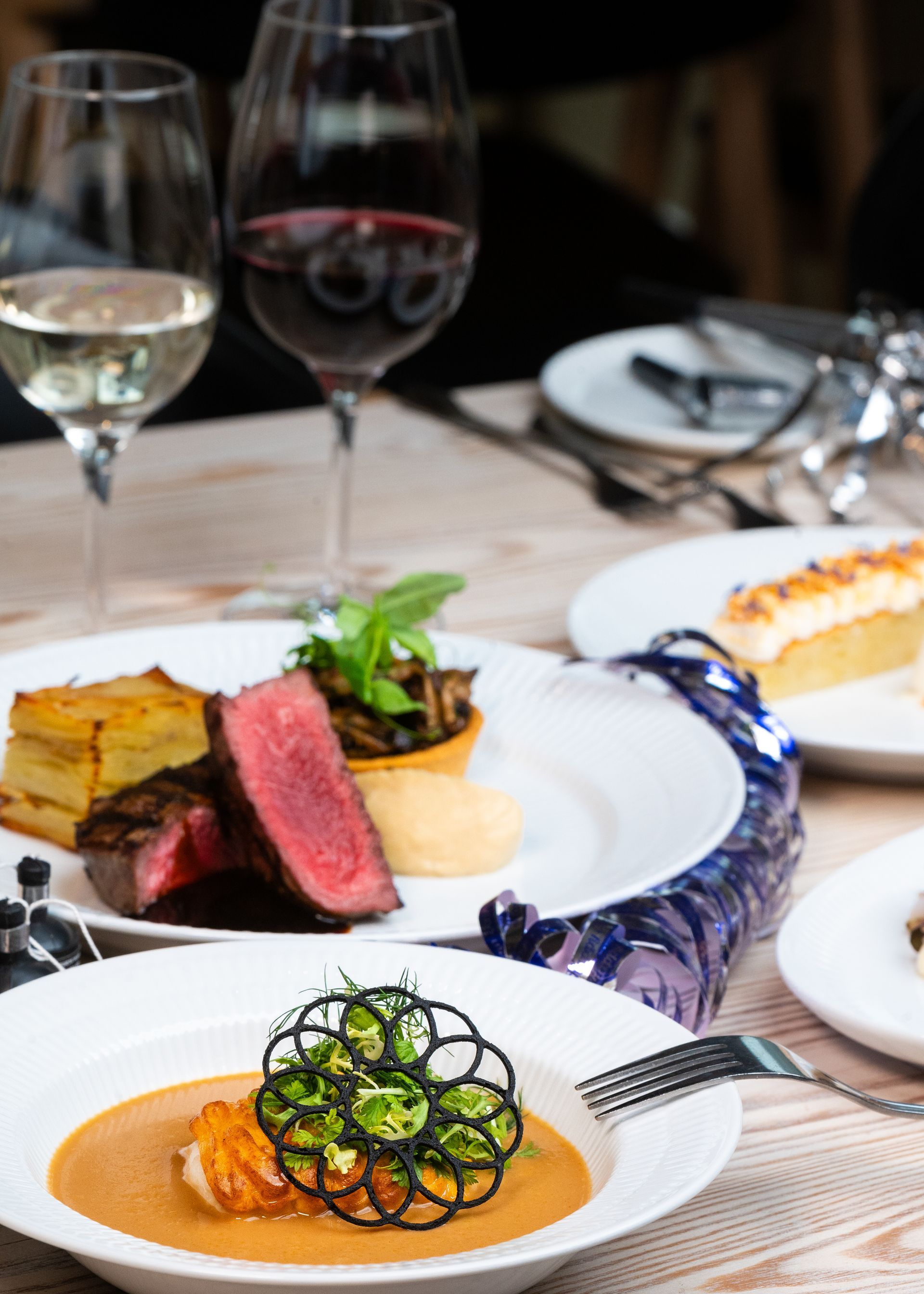 Gourmetretter med rød- og hvidvinsglas på et restaurantbord; bøf, suppe, tilbehør.