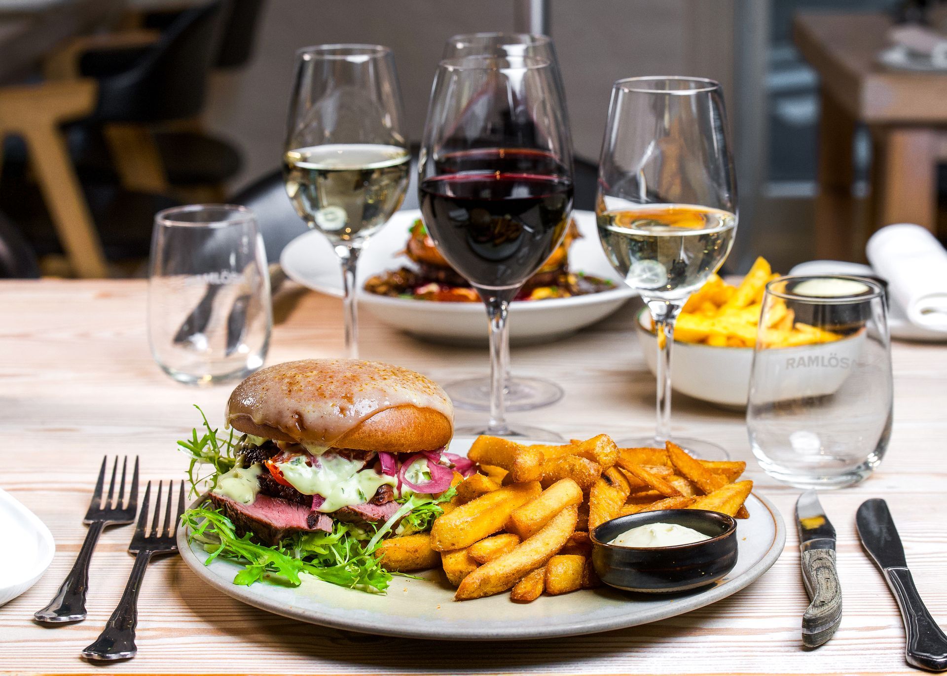 Burger med pommes frites og vinglas på et restaurantbord.