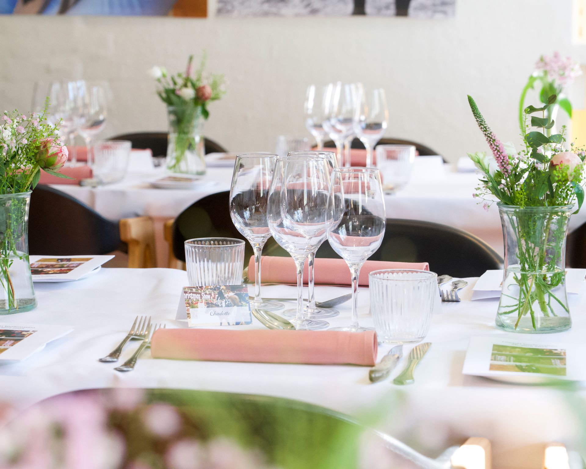 Borddækning med glas, blomster og lyserøde servietter i en lys spisestue.