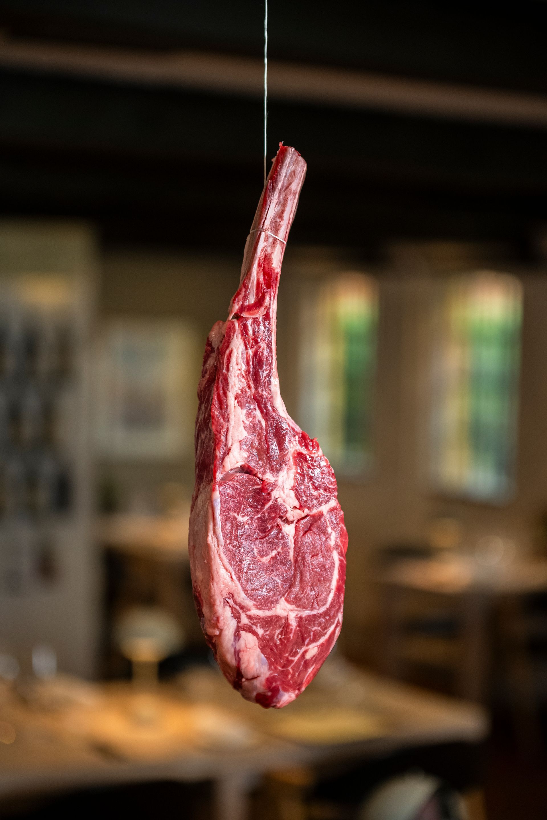 Rå tomahawk-bøf ophængt i en snor på en restaurant.