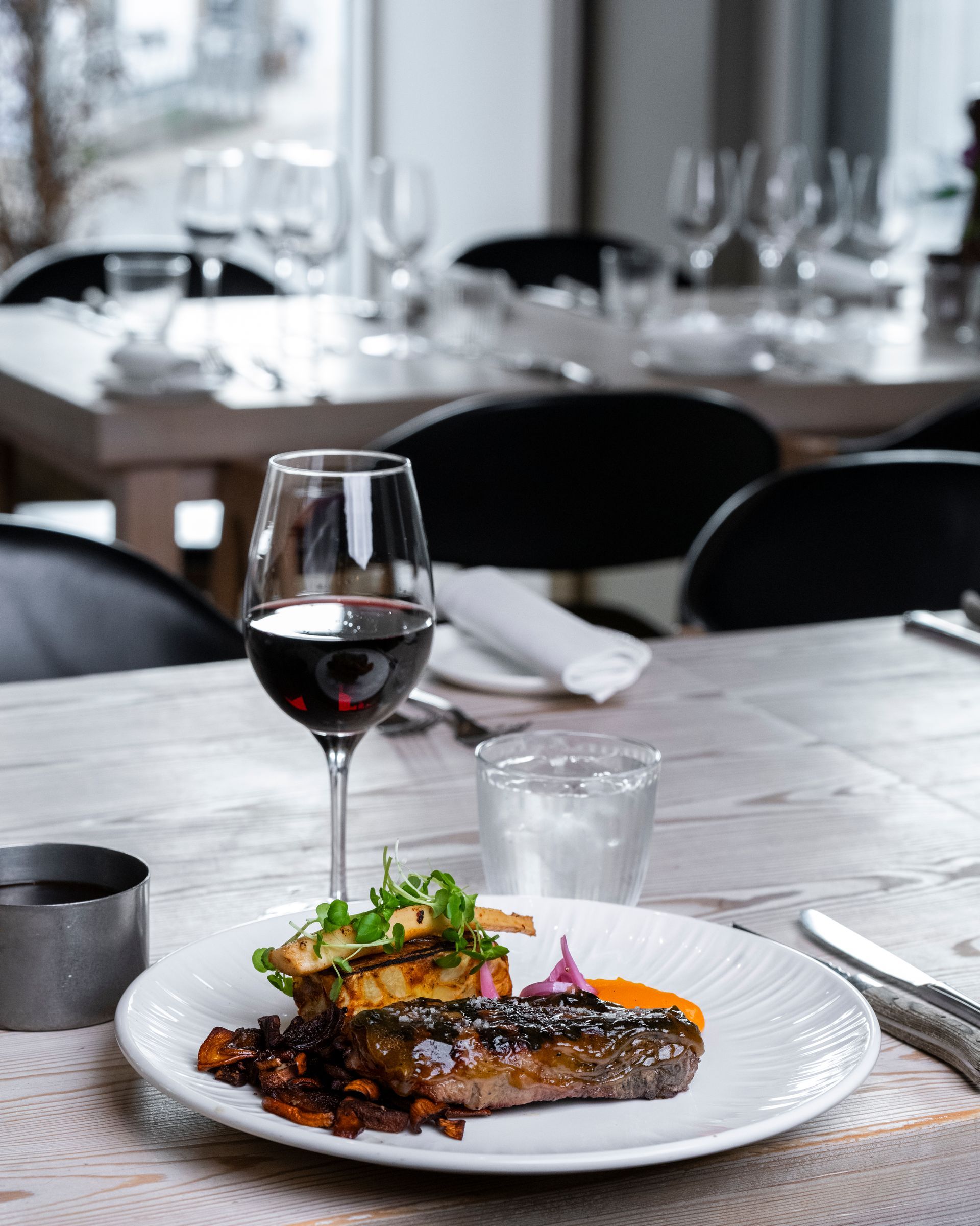 Bøfmiddag med rødvin, vandglas og bestik på et rustikt træbord i en restaurant.