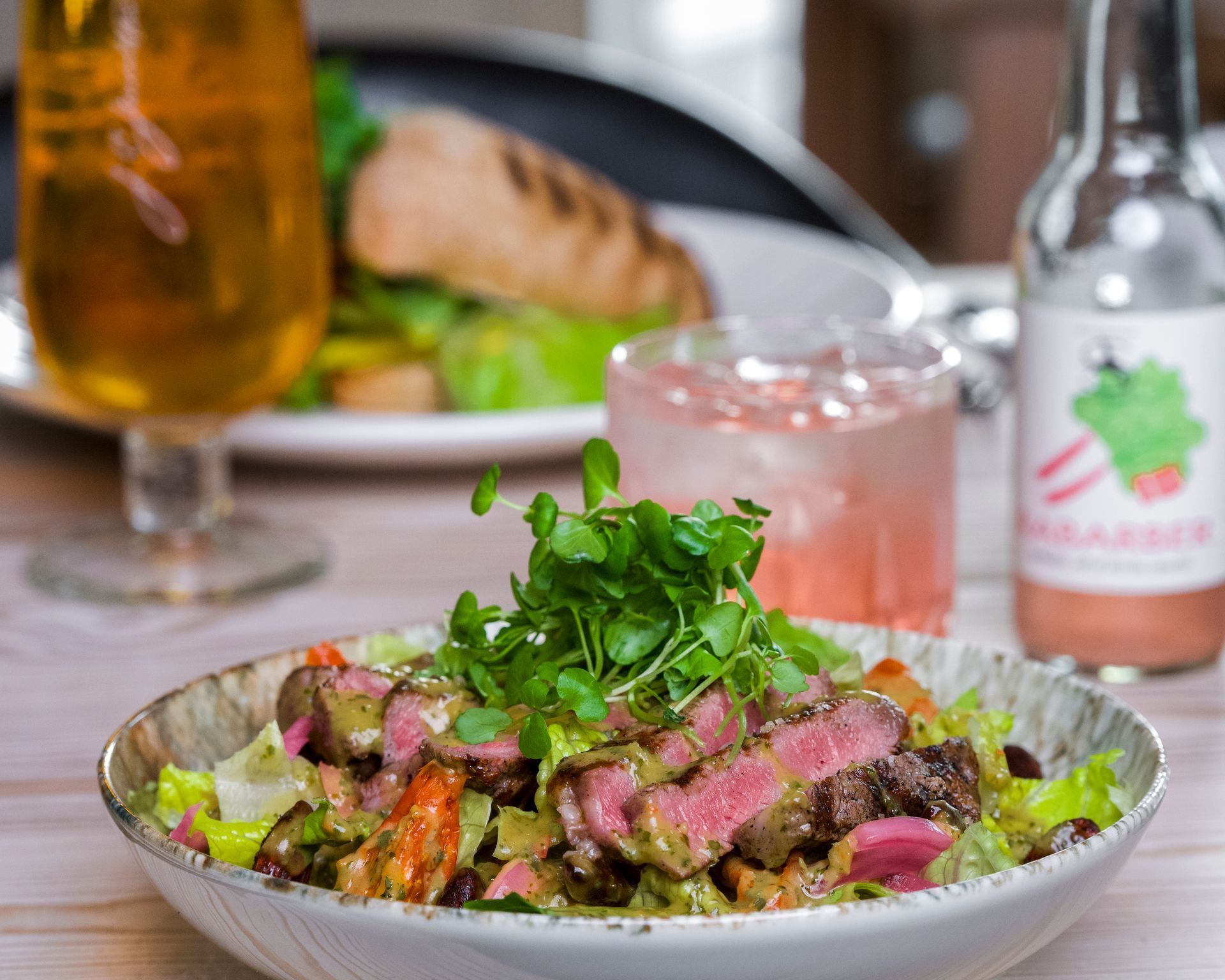 Bøfsalat med friske grøntsager, ved siden af ​​drikkevarer og en tallerken grillet laks.