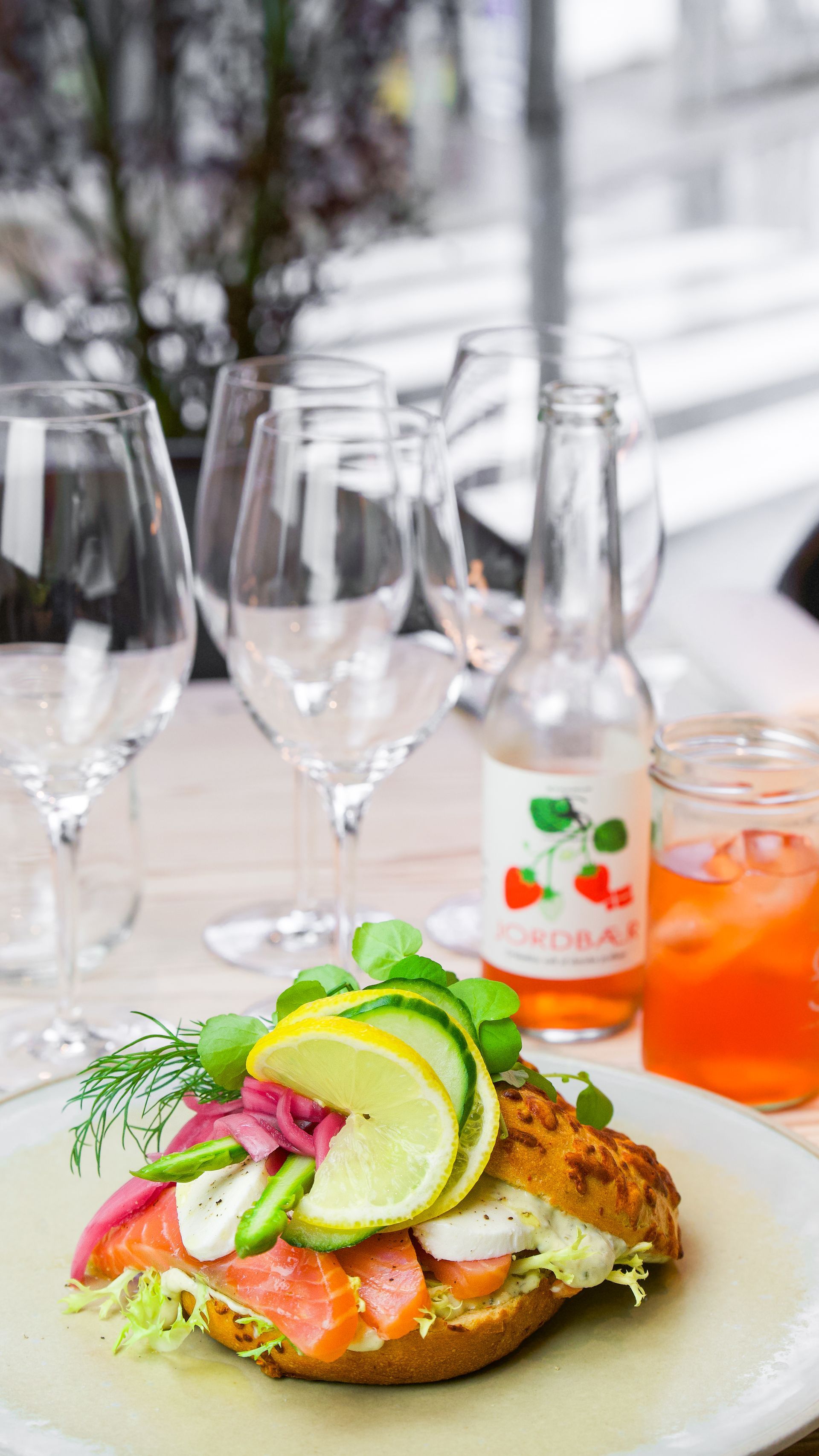 Røget laks toast toppet med grøntsager, lime og radiser. Vinglas, sodavandsflaske og juice.