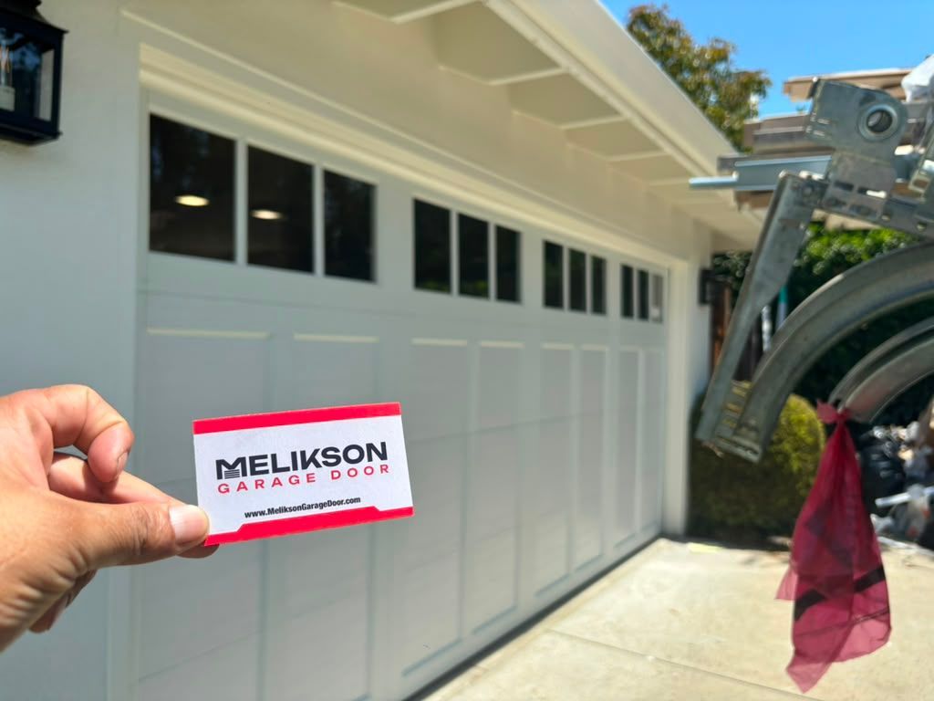 Melikson Garage Door business card held in front of a white carriage-style garage door