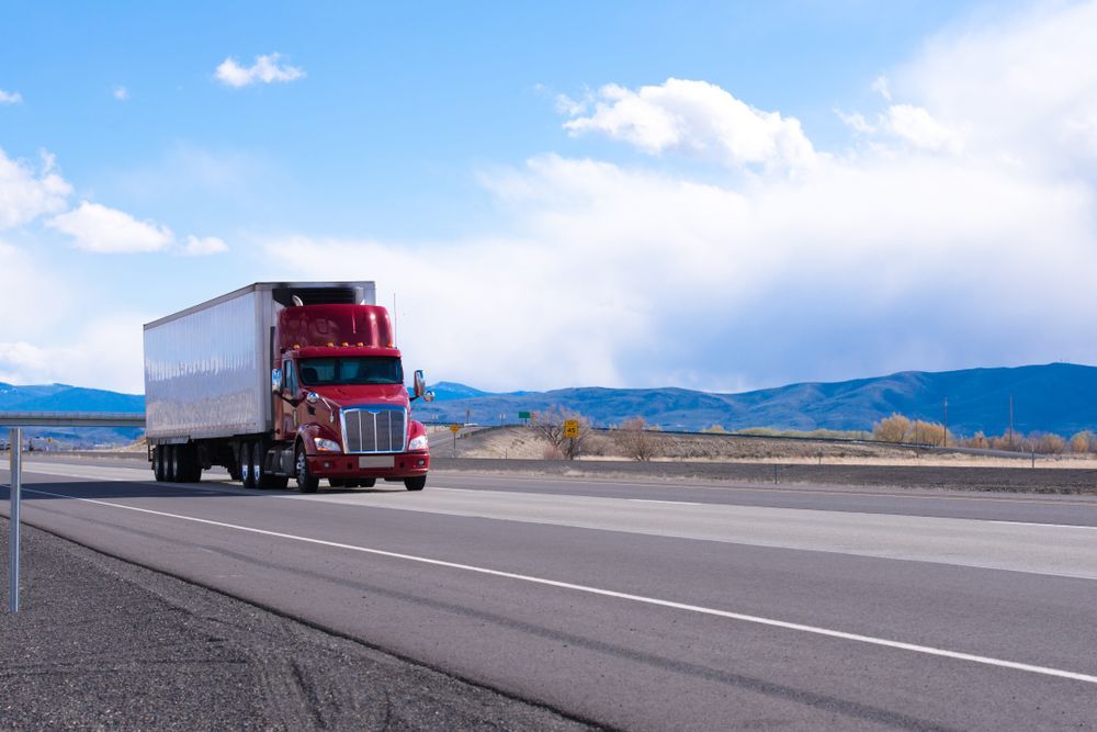 A Red Semi Truck Is Driving Down A Highway With Mountains In The Background — Gillies Enterprises Pty Ltd In Moree, NSW