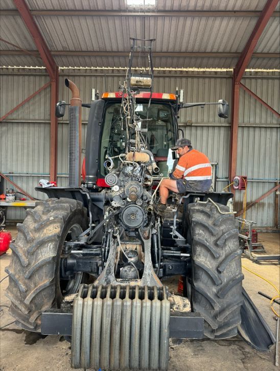 A Man Is Working On A Tractor In A Garage — Gillies Enterprises Pty Ltd In Coonabarabran, NSW