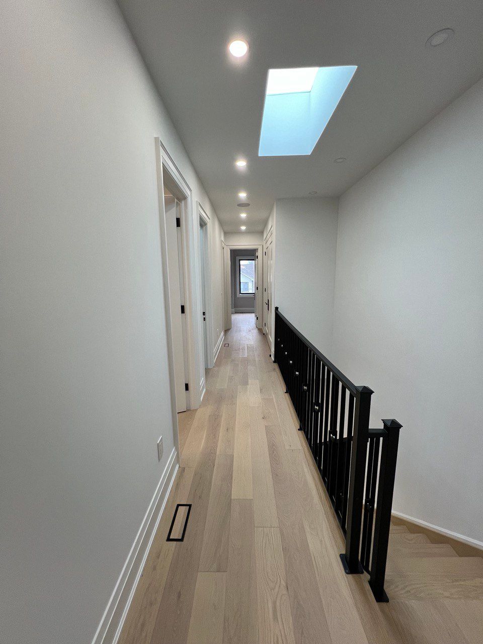 A long hallway with hardwood floors and a skylight in the ceiling.