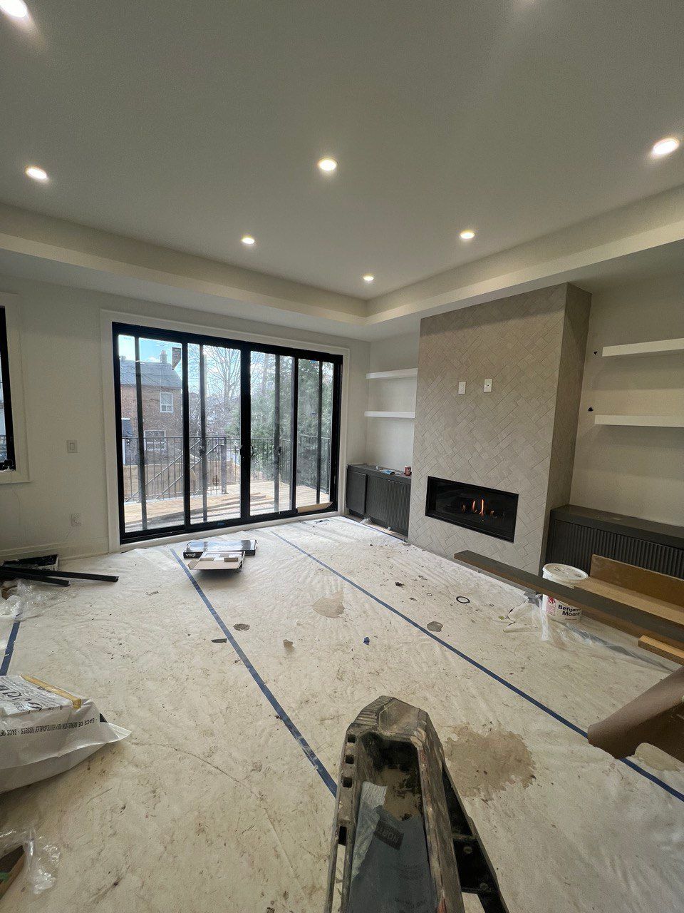 A living room with a fireplace and sliding glass doors is being remodeled.