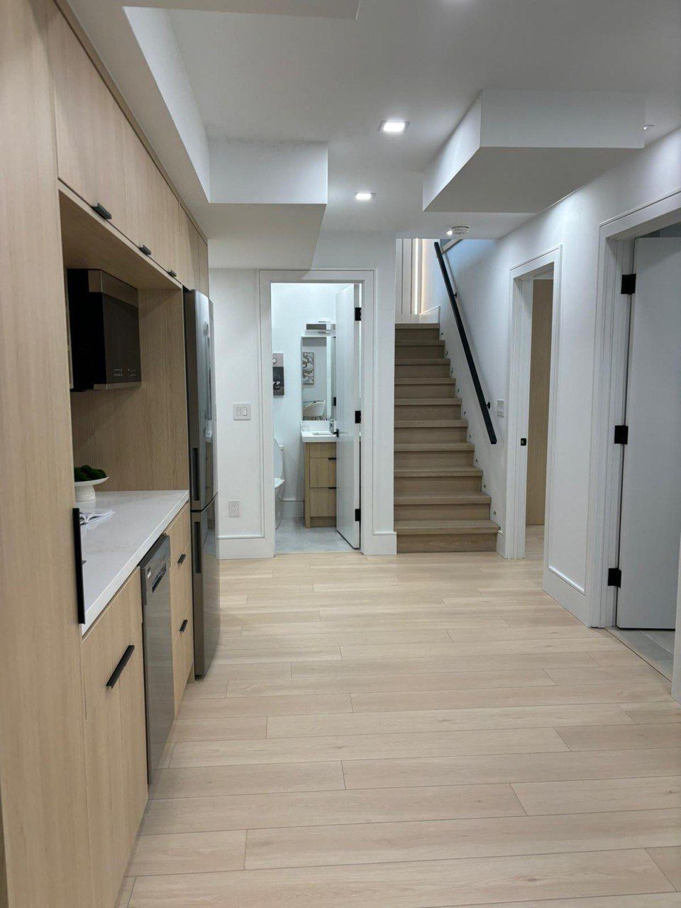 A kitchen with wooden cabinets , stainless steel appliances , a refrigerator and stairs.