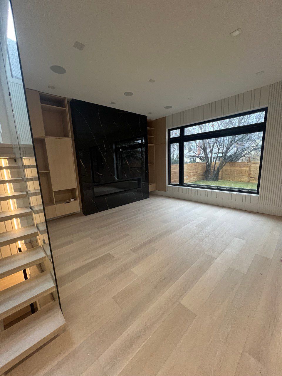 A living room with hardwood floors , stairs , a fireplace and a large window.