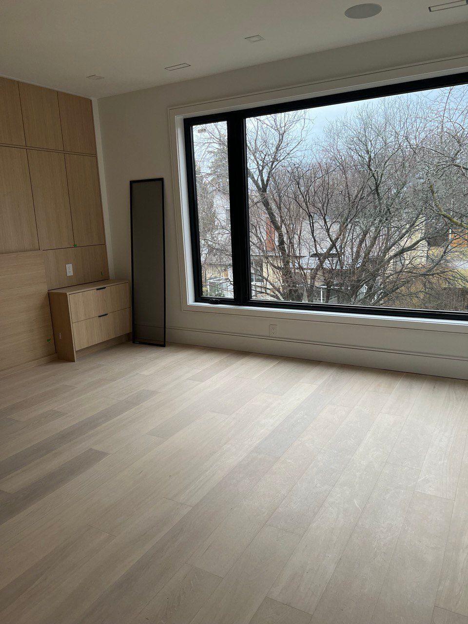 An empty room with a large window and a wooden floor.