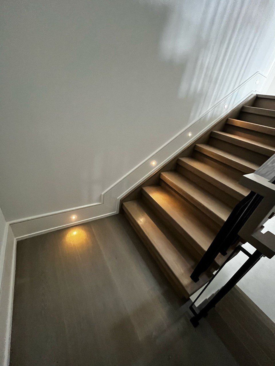 A wooden staircase with lights on the steps in a house.