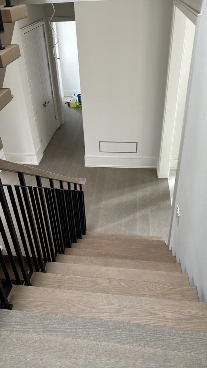 A wooden staircase with a black railing leading up to a hallway.