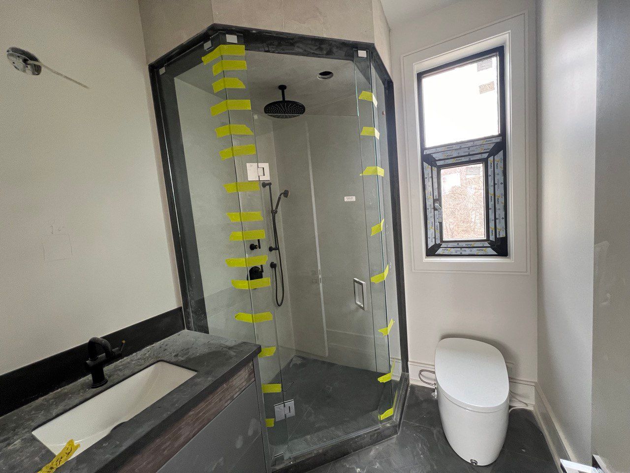 A bathroom with a toilet , sink , shower and window.