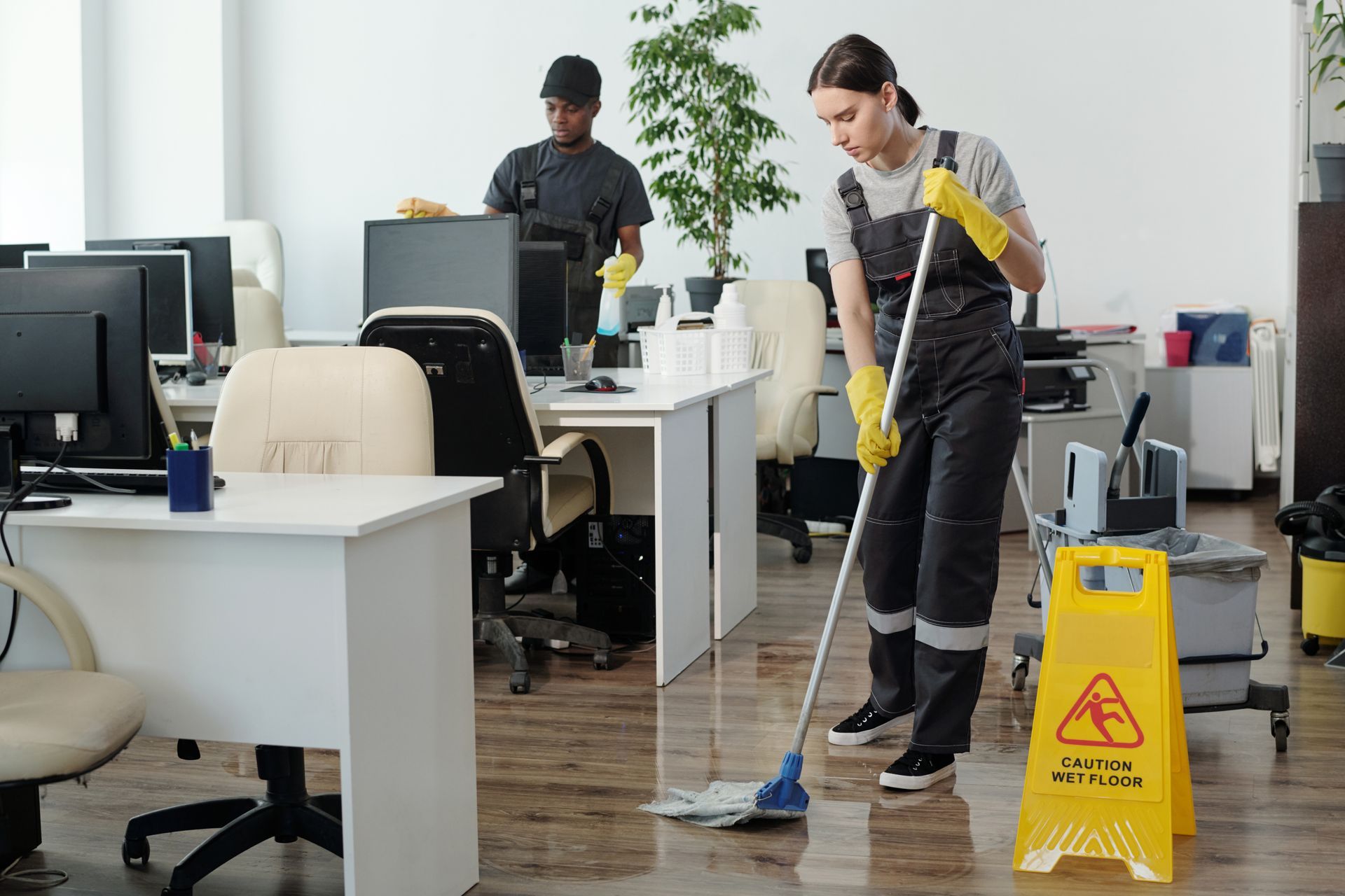 A woman is cleaning the floor of an office with a mop.