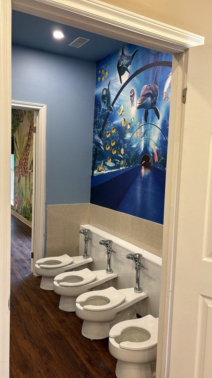 A row of toilets in a bathroom with a mural on the wall.