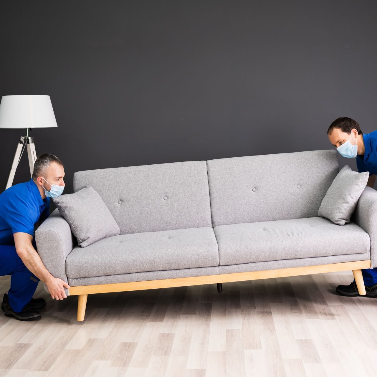 two men wearing face masks are moving a couch
