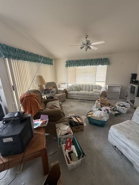 Cluttered living room with furniture, boxes, and bags around a couch near bright windows