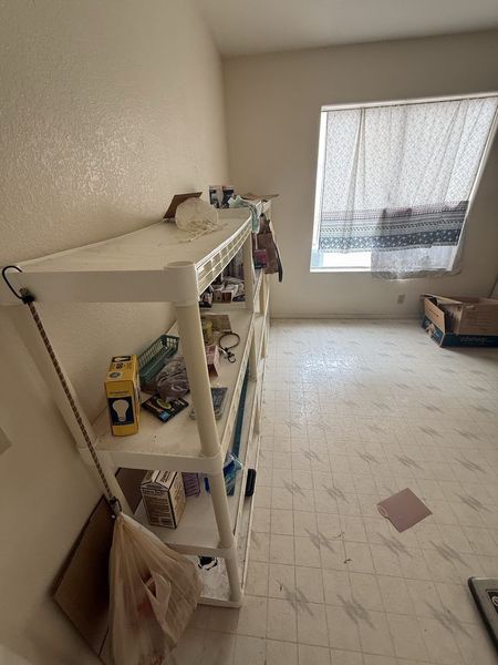 Small empty room with white shelves, a window with lace curtains, and a tiled floor.