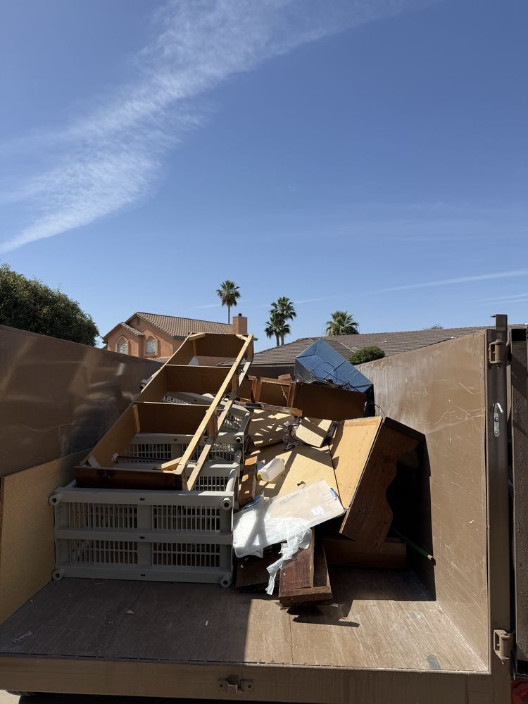 Overflowing dumpster with discarded furniture and debris under a clear blue sky