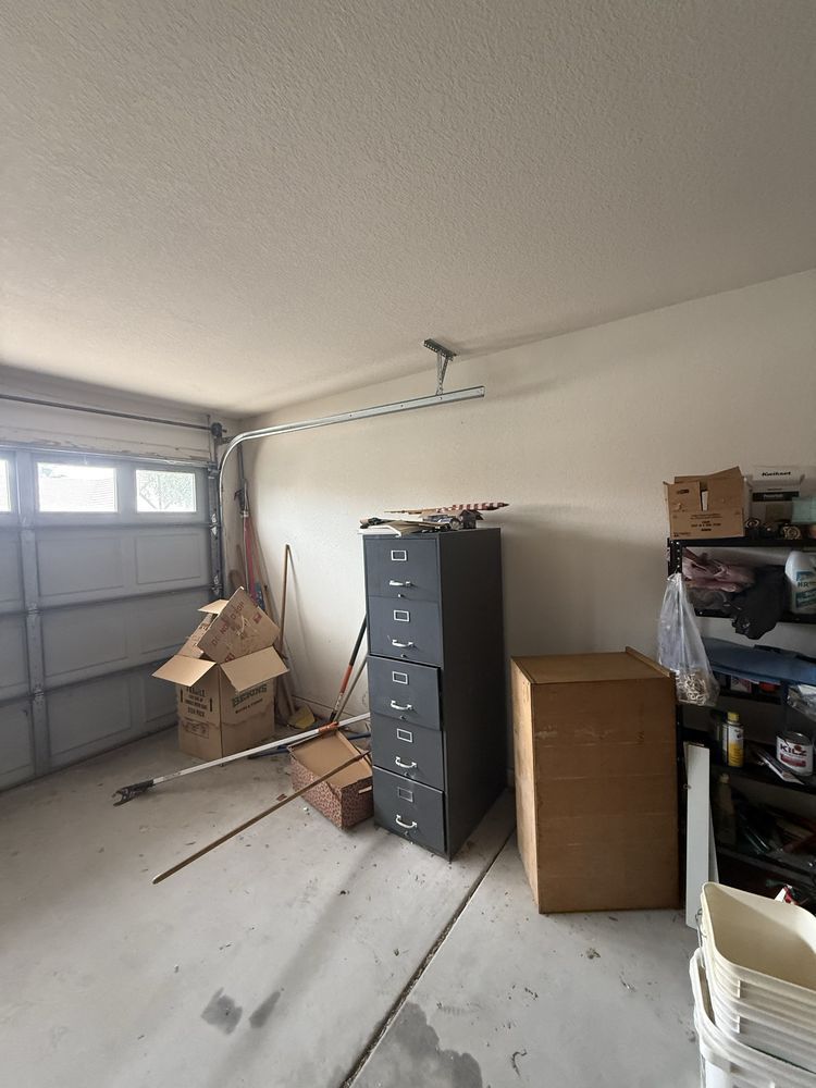 Garage interior with a gray filing cabinet, cardboard boxes, and stored items along the wall.
