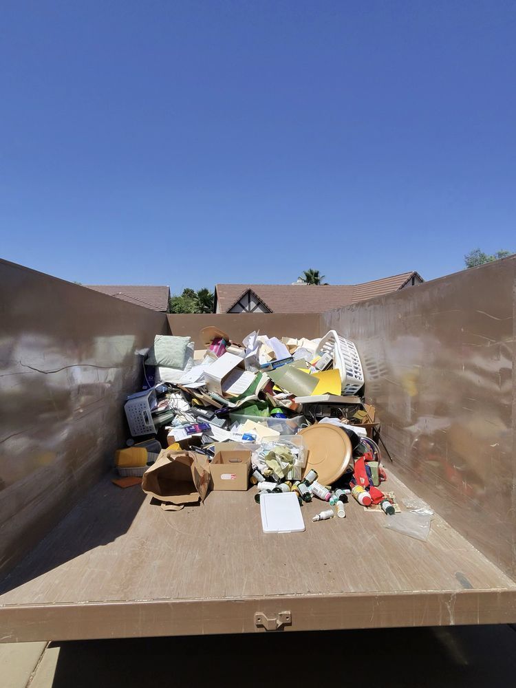 Open dumpster filled with assorted trash and debris under a clear blue sky