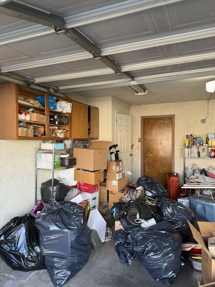 Cluttered garage with many black trash bags, stacked boxes, and shelves under a metal ceiling