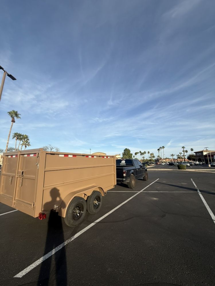 Black trailer hitched to a blue vehicle in a parking lot under a bright blue sky
