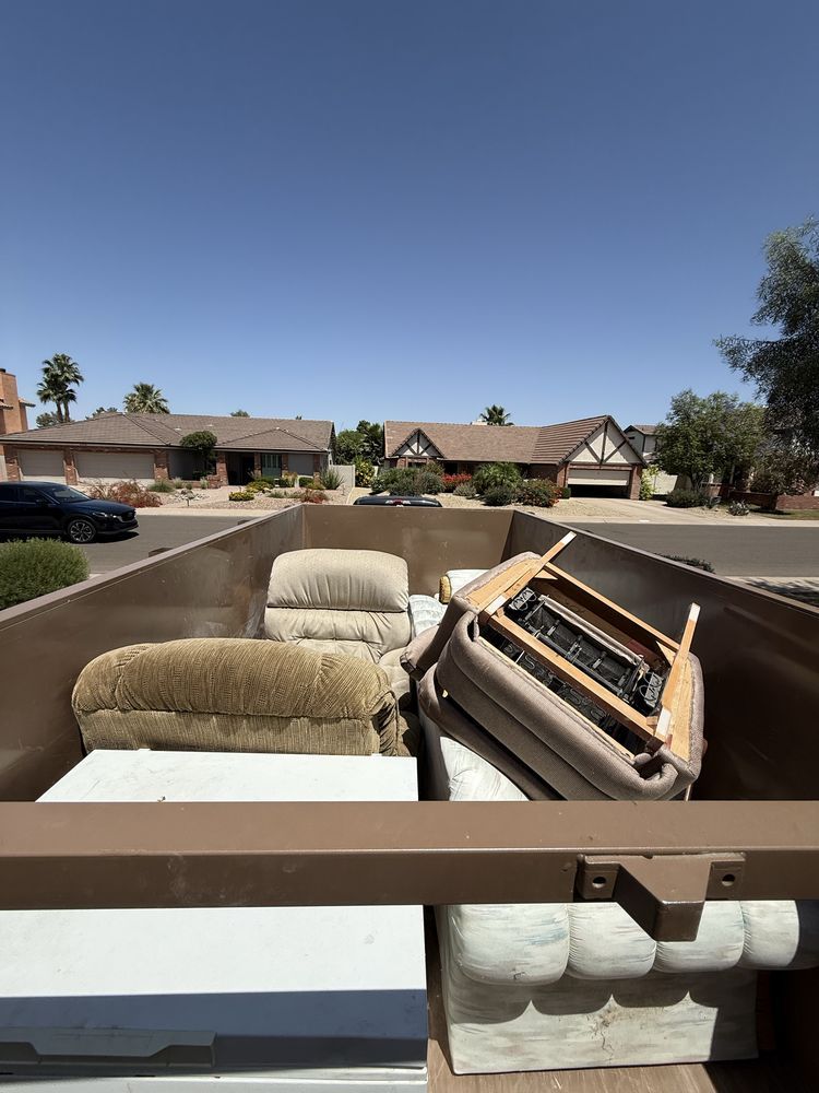 Furniture and a mattress piled in a moving truck against a sunny suburban neighborhood.