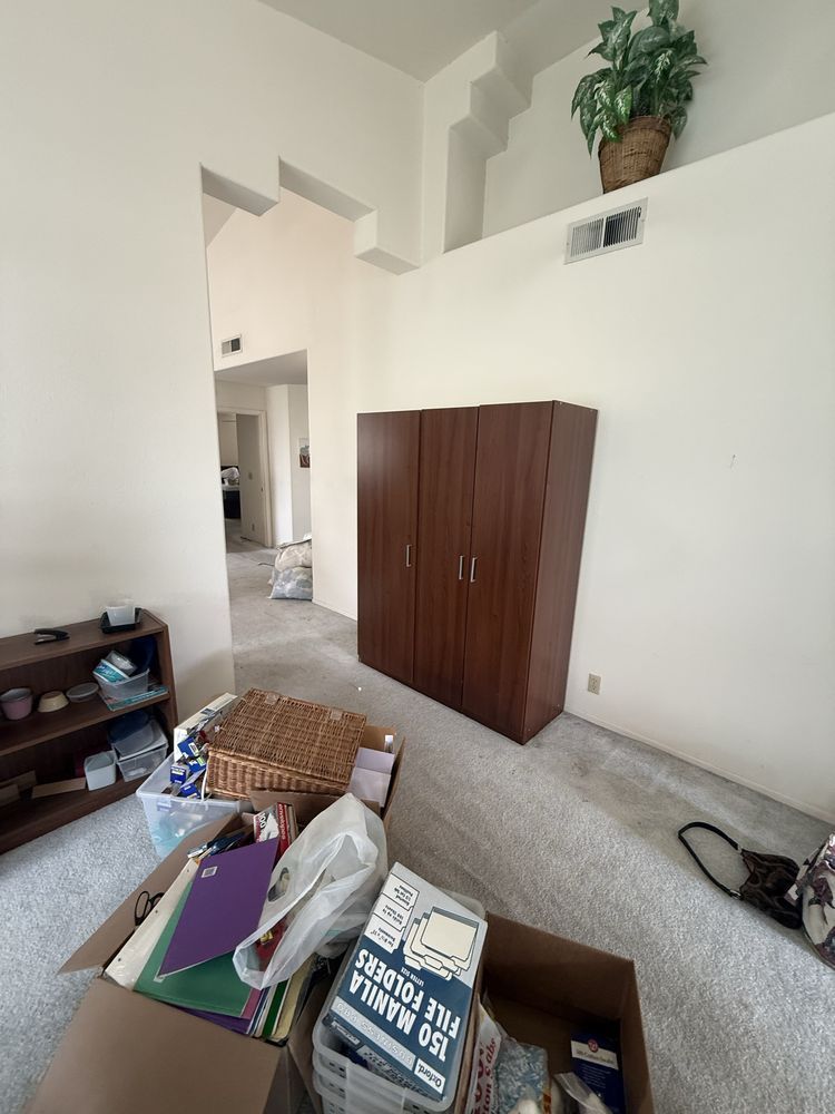 Scattered boxes and baskets in a room with a wooden wardrobe, high ceiling, and open doorway