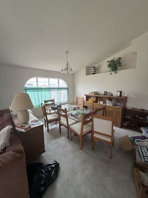 Dining room with wooden table and chairs, sideboard, lamp, and arched window with green curtains