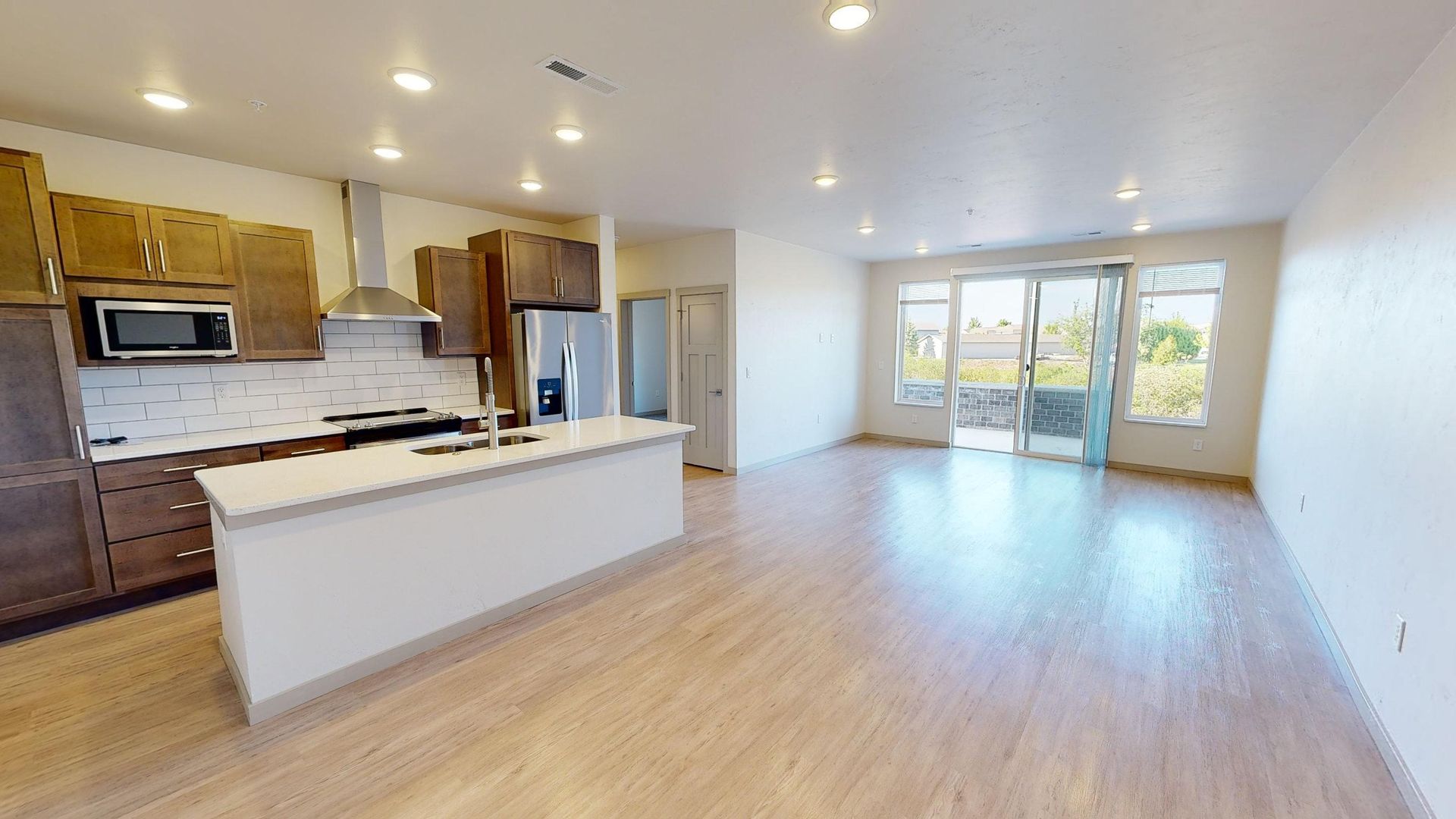 Bright open kitchen and living area with white island, wood cabinets, and sliding glass doors to a patio