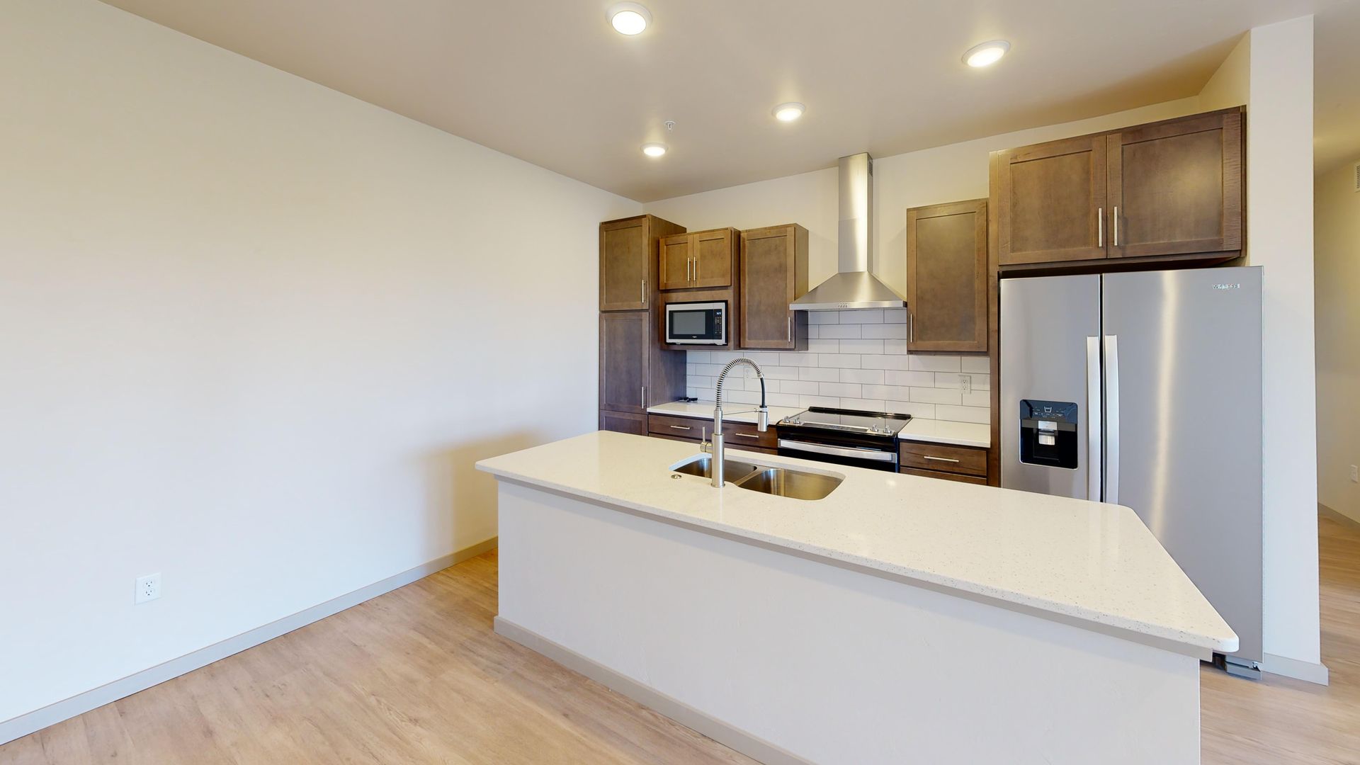 Modern kitchen with white island, wood cabinets, stainless steel appliances, and light wood flooring
