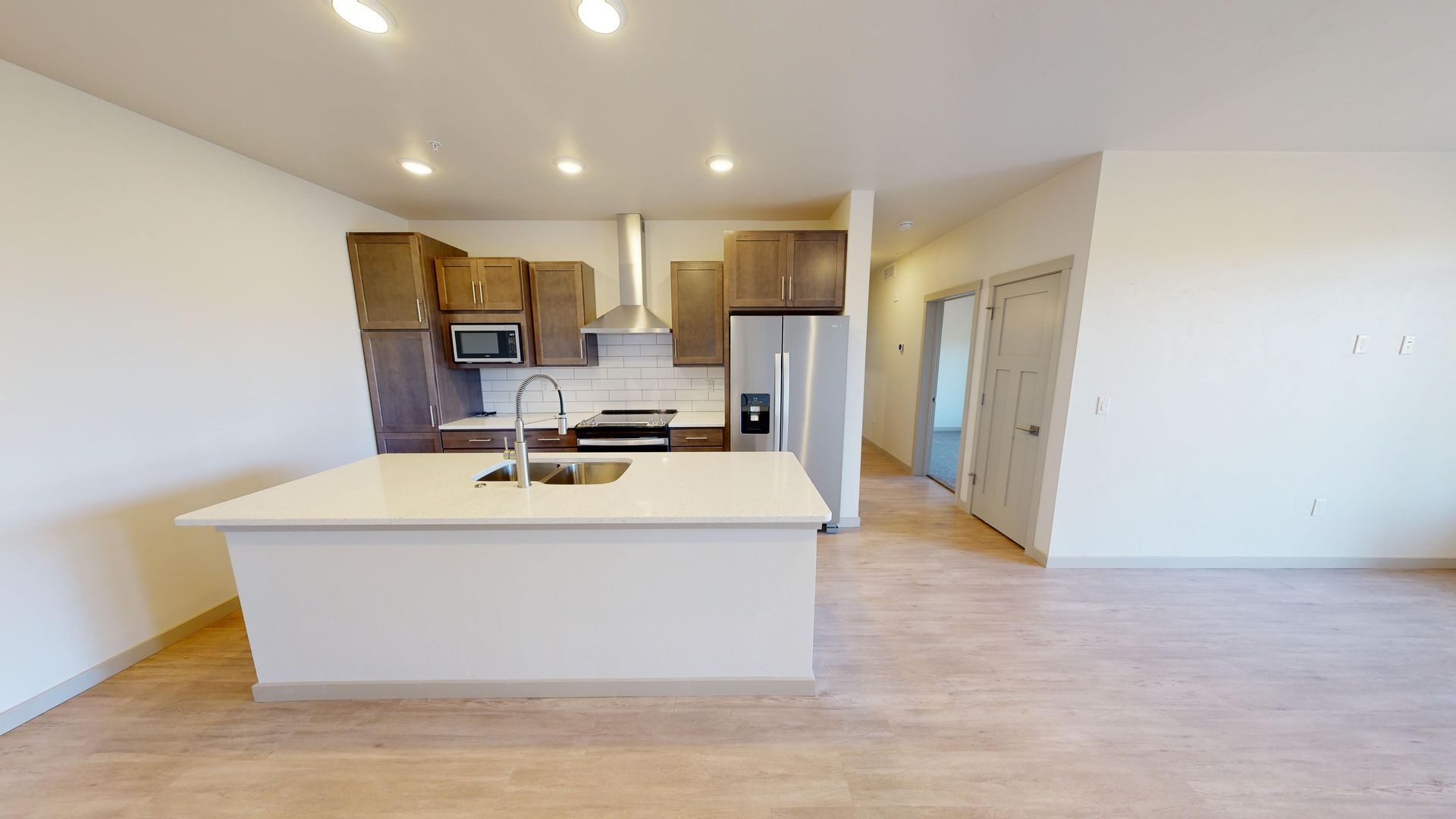 Open-plan kitchen with white island, wood cabinets, stainless appliances, and light wood floors