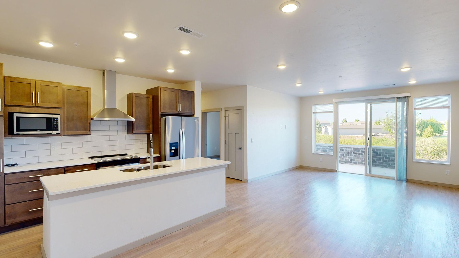 Bright open kitchen and living area with wood floors, white cabinets, and sliding glass doors to a balcony.