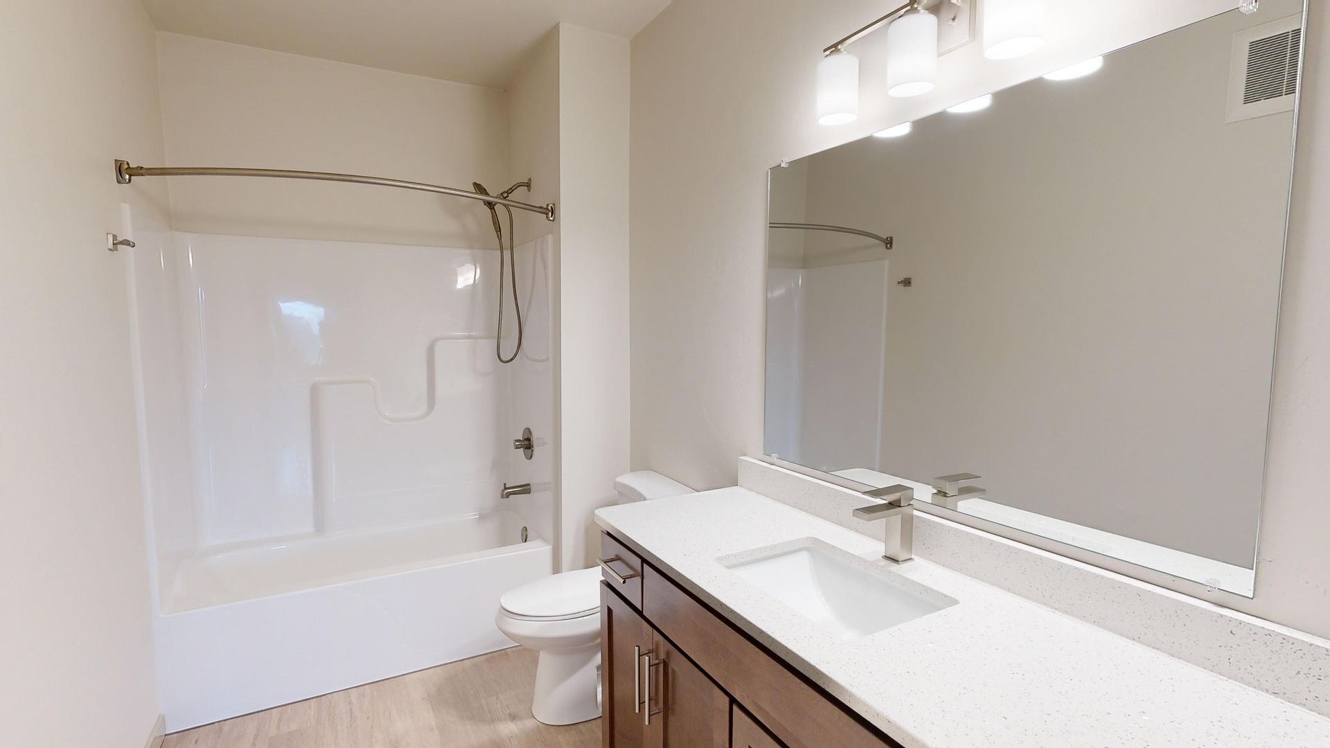 Bright bathroom with white tub, large mirror, vanity, and neutral tile walls.
