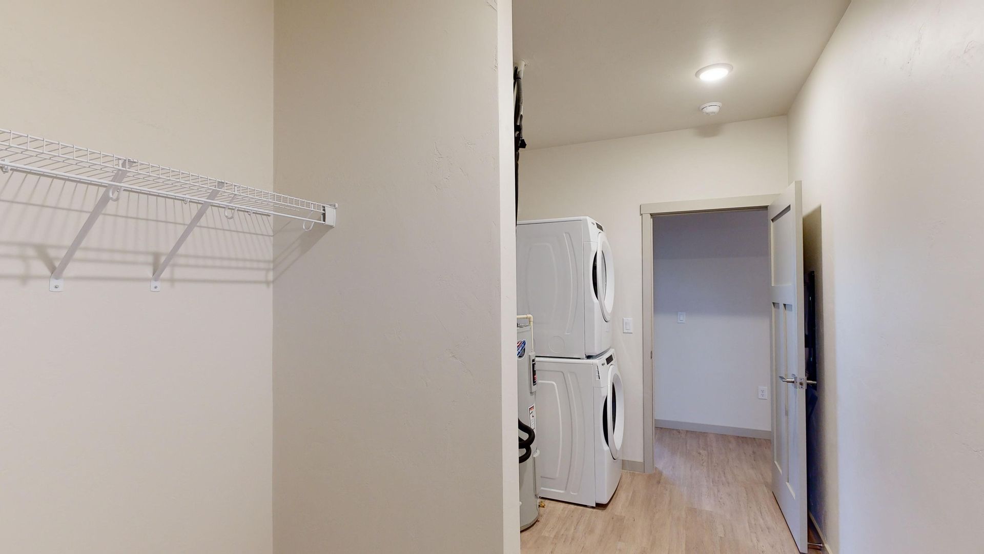 Narrow white hallway with a wire shelf, refrigerator at the end, and an open doorway to the right.