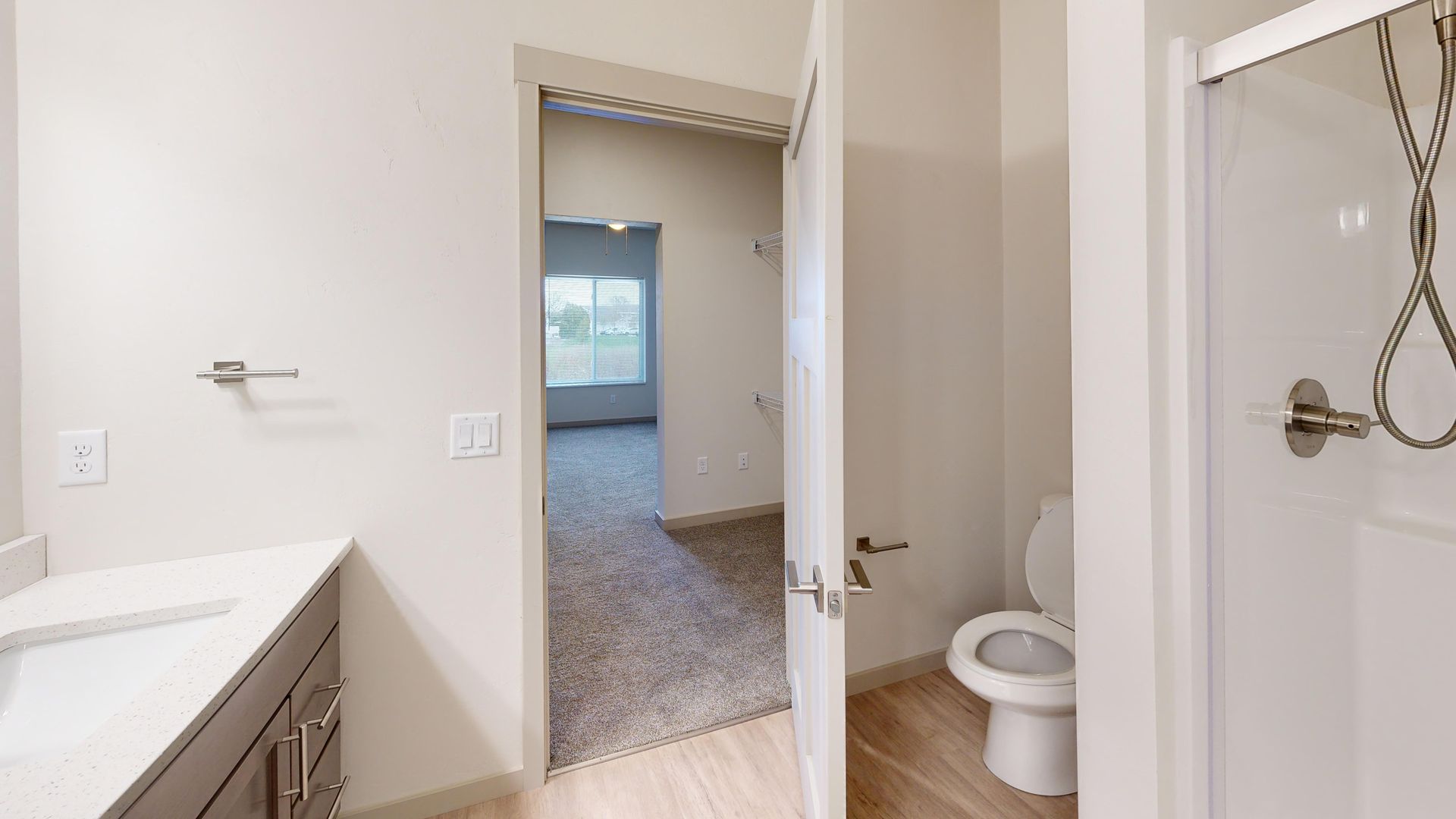 Bathroom with white vanity, open door to a carpeted room, and a toilet visible in an adjoining bath area