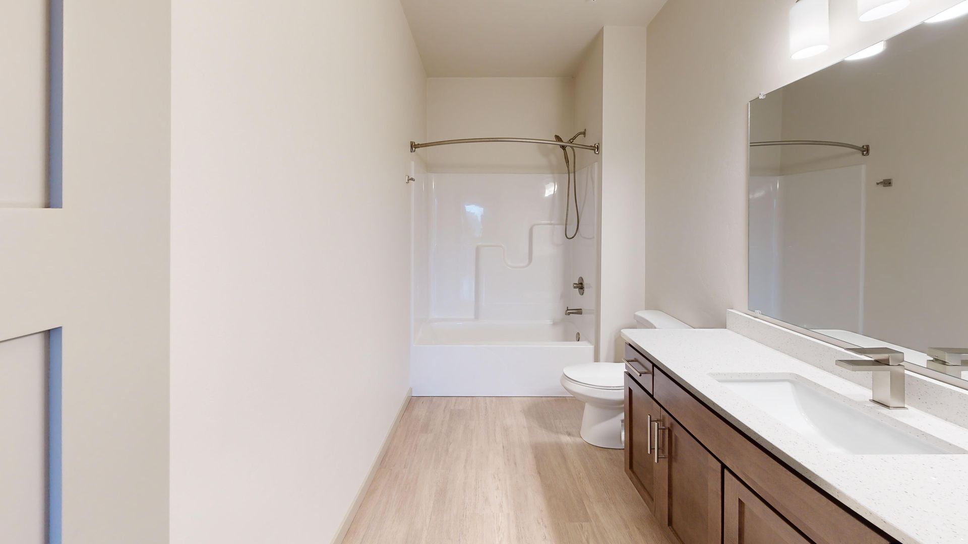 Bright bathroom with long vanity, large mirror, and a white tub shower at the far end.