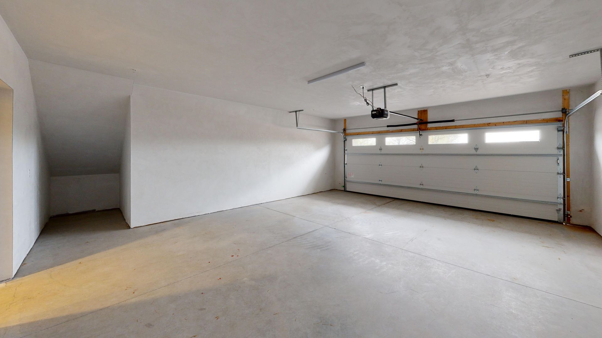 Empty two-car garage with white walls, concrete floor, and a closed garage door.