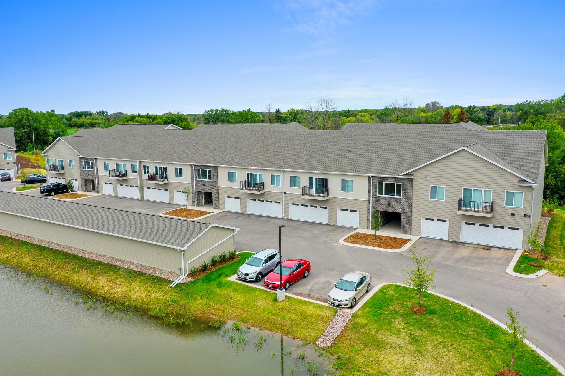 Apartment building with balconies, white siding, and a manicured lawn on a sunny day