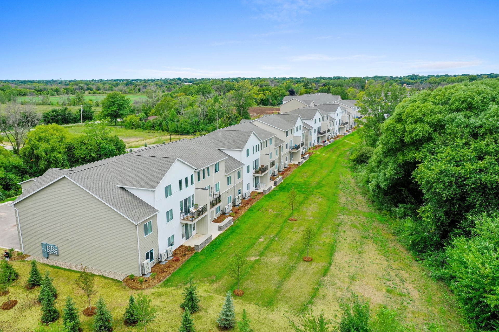 Aerial view of white apartment buildings beside a grassy field and dense green trees